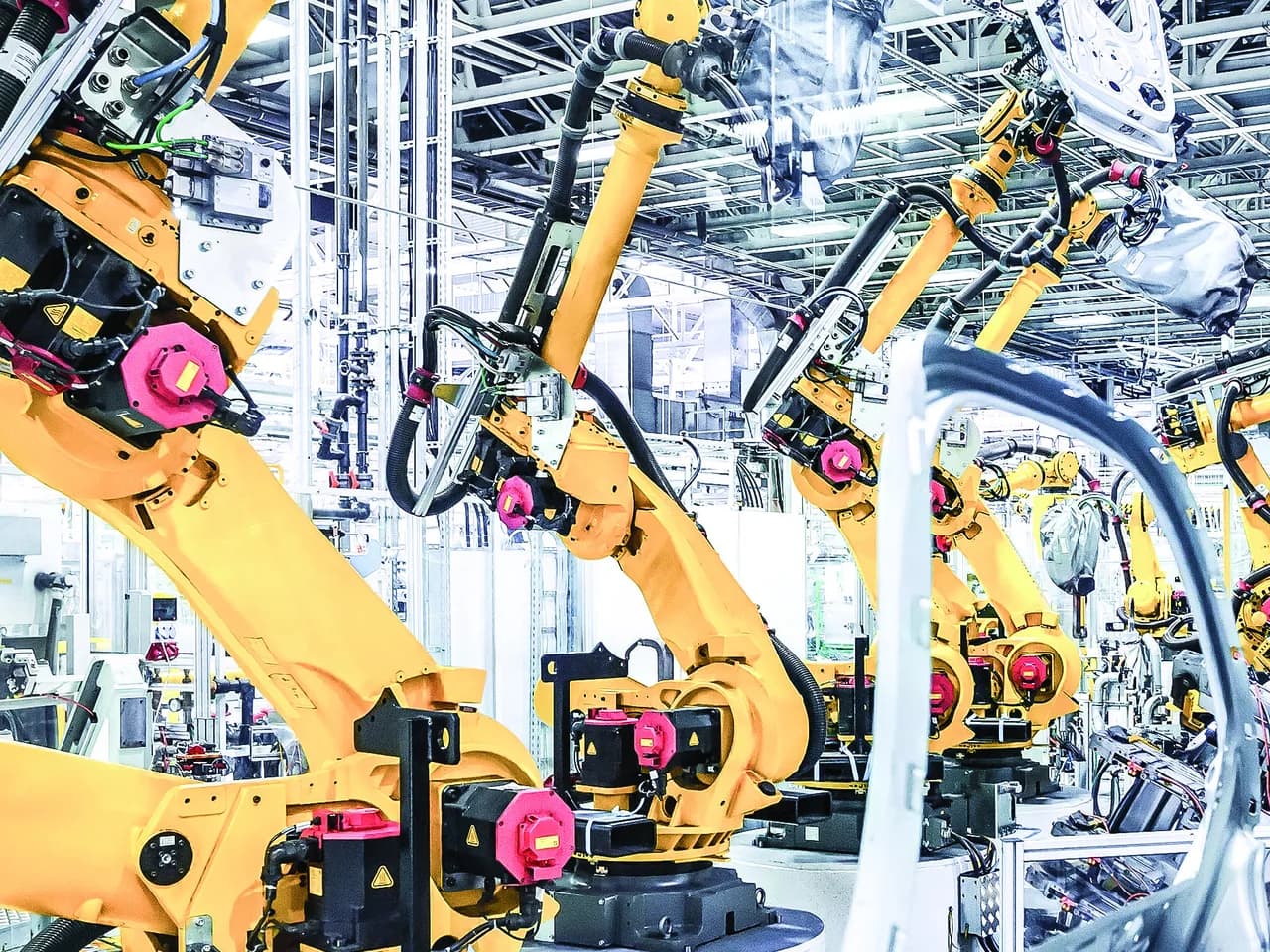 Yellow industrial robots handling vehicle body panels on an automotive assembly line