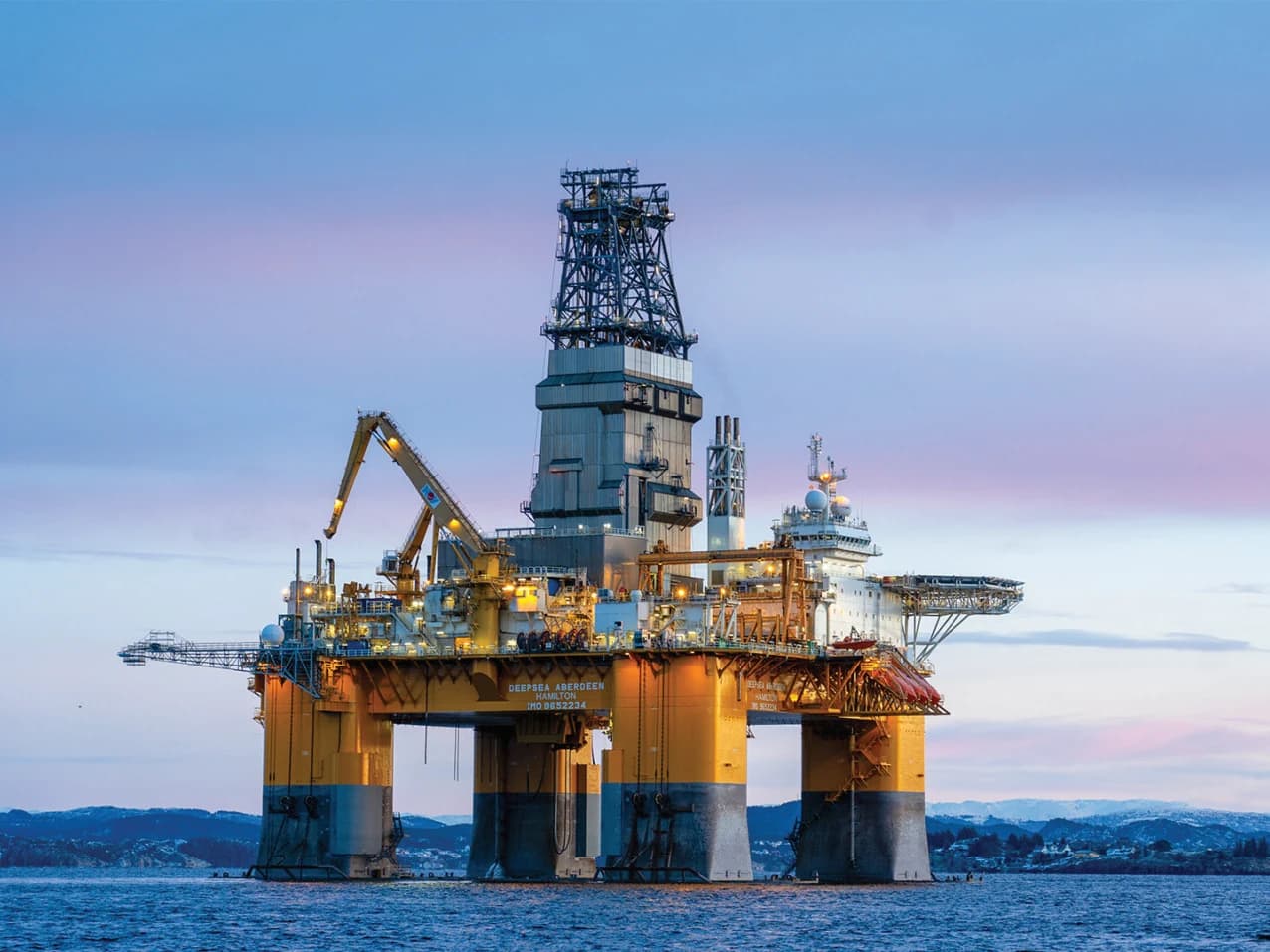 Offshore drilling installation with a tall derrick, cranes and illuminated deck equipment
