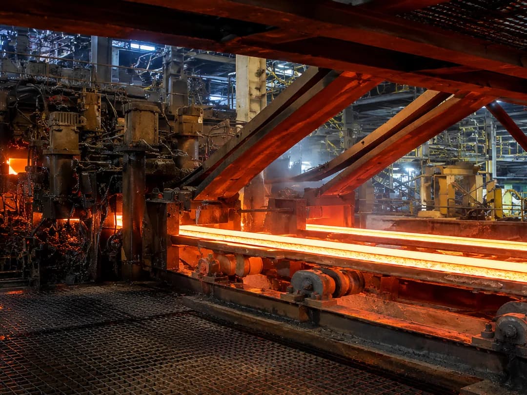 Glowing steel moving through industrial rolling equipment